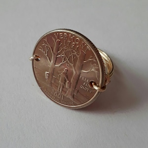 May include: A silver US quarter coin with the Vermont state quarter design, featuring a maple sugaring scene, is mounted on a gold wire ring. The coin is dated 2001 and reads "VERMONT 1791" and "E PLURIBUS UNUM".