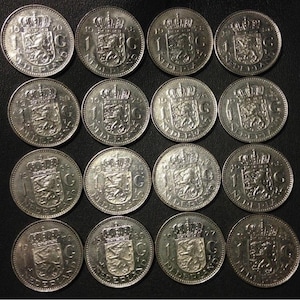 May include: Sixteen silver Dutch coins, each featuring a crowned lion rampant within a shield, the text "1 NEDERLAND" and the year of minting. The coins are arranged in four rows of four on a dark surface.