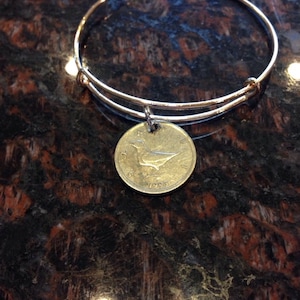 May include: A silver bangle bracelet with a Canadian one dollar coin charm featuring a bird design and the year 1995.