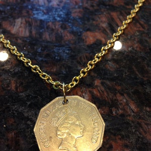 May include: A gold chain necklace with a gold coin pendant featuring a profile of Queen Elizabeth II and the text "Queen Elizabeth the Second".