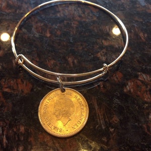 May include: A gold bangle bracelet with a gold coin charm. The coin has the words "KONINGIN BEATRIX DER NEDERLANDEN" inscribed around the edge.