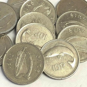 May include: A collection of Irish coins, including 10p coins, with various designs. The coins are silver in color and feature images of a fish, a harp, and the word "eire". The coins are scattered across a surface.