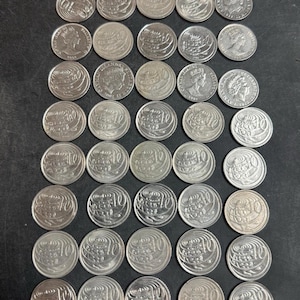 Può includere: Una collezione di trentacinque monete color argento disposte in una griglia. Ogni moneta presenta il numero 10 o un ritratto della regina Elisabetta II. Le monete sono circolari con superfici metalliche e varie iscrizioni.