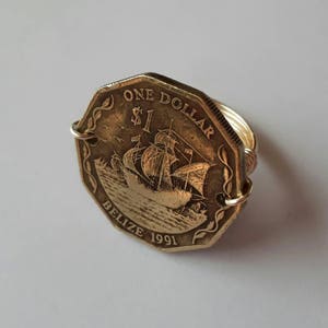 May include: A unique ring made from a Belize one-dollar coin from 1991. The coin, with its sailing ship design, is set in a gold-coloured wire band. The ring's design is octagonal, offering a distinctive and artistic look.