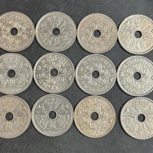 May include: A collection of twelve silver-colored Danish 2 Kroner coins arranged in a grid. Each coin features a central hole, a crown, and heart motifs. The text 2 KRONER DANMARK is embossed on the coins, with various production years visible.
