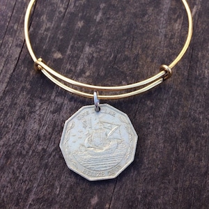 May include: A gold bangle bracelet with a silver Belizean dollar coin charm featuring a ship and the text "ONE DOLLAR BELIZE 2005".