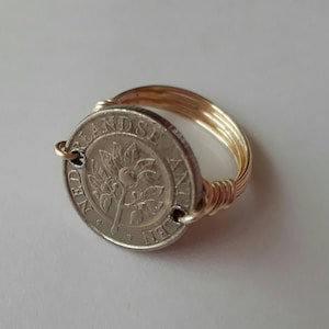 May include: A gold wire wrapped ring with a Dutch coin featuring a tree and the text "NEDERLANDSE ANTILLEN" on the front.