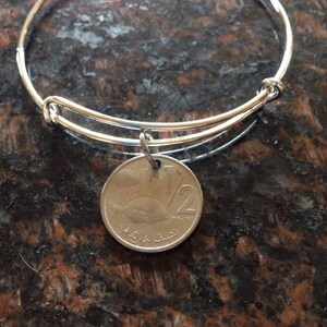 Könnte beinhalten: Ein silbernes Armreif-Armband mit einem silbernen Anhänger. Der Anhänger ist eine runde Münze mit der Zahl "1/2" und dem Text "جمهورية مصر العربية" in arabischer Schrift.