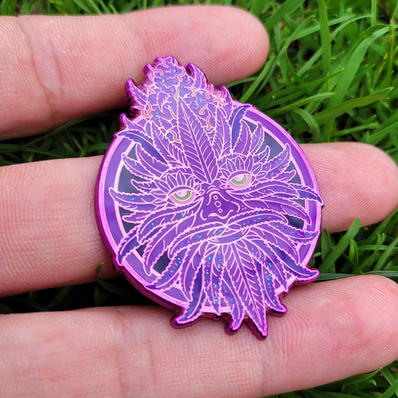 K&ouml;nnte beinhalten: Eine violette und gr&uuml;ne Emaille-Anstecknadel mit einem fantasievollen gr&uuml;nen Mann mit einem Blatt-Bart und einer Krone aus Bl&auml;ttern. Die Anstecknadel hat eine glitzernde Oberfl&auml;che.