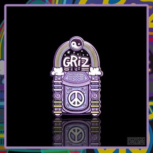 May include: A purple and white enamel pin in the shape of a jukebox. The pin features the word "GRIZ" in white, a rainbow, a peace sign, and a yin-yang symbol. The pin has a black background and a colourful border.