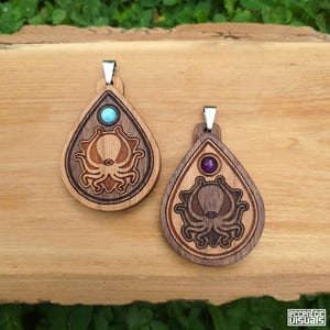 Puede incluir: Dos colgantes de madera con un diseño de pulpo. Un colgante tiene una piedra turquesa, el otro una piedra púrpura. Los colgantes tienen forma de lágrima con una fianza plateada. El diseño del pulpo está tallado en la madera.
