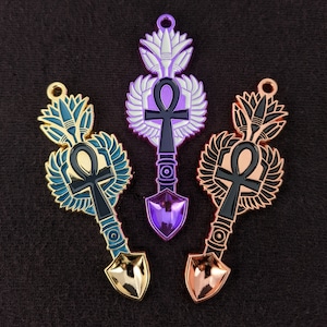 May include: Three gold-tone metal keychains featuring an ankh symbol and wings. The keychains are in purple, blue and gold.