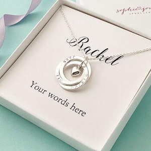 May include: Silver necklace featuring three interlocked circles and a small heart charm. The circles are engraved with the words "First", "Last", and "Name". The necklace is presented in a white box with the name "Rachel" inscribed on it.
