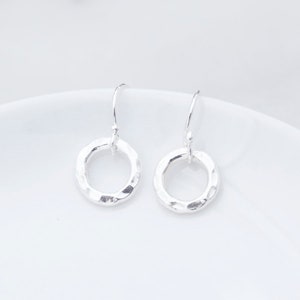 May include: A pair of silver hammered circle dangle earrings. The earrings are simple and elegant, and would make a great gift for any occasion.