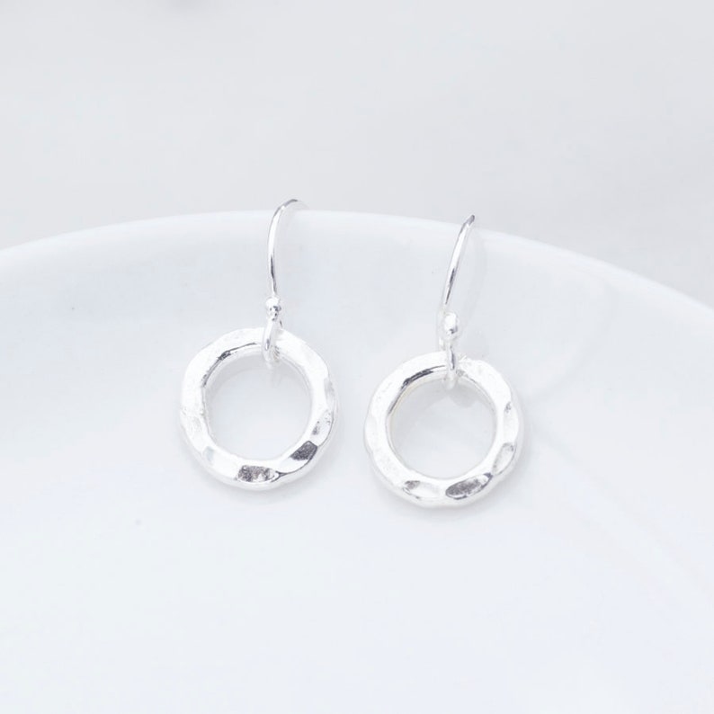 May include: A pair of silver hammered circle dangle earrings. The earrings are simple and elegant, and would make a great gift for any occasion.