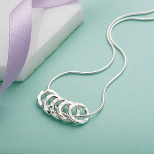 May include: A silver necklace with five interconnected hammered rings. The necklace is on a light blue background.