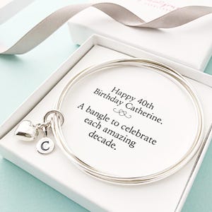 May include: A silver bangle bracelet in a white gift box, with a heart charm and a letter "C" charm. The card reads "Happy 40th Birthday Catherine. A bangle to celebrate each amazing decade."