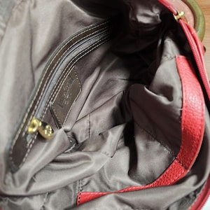 May include: A red handbag with a textured exterior and a dark brown fabric interior lining. The interior features a zippered pocket with a gold-toned metal pull and a rectangular leather patch embossed with the brand name Luv Betsey.