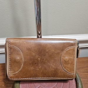 May include: A brown leather wallet with a zipper closure and two decorative stitching details on the front.