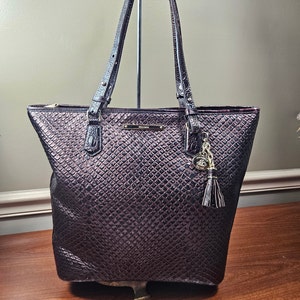 May include: A dark brown leather tote bag with a snakeskin pattern. The bag has a zipper closure and two top handles. A gold-tone charm with a tassel hangs from the bag.