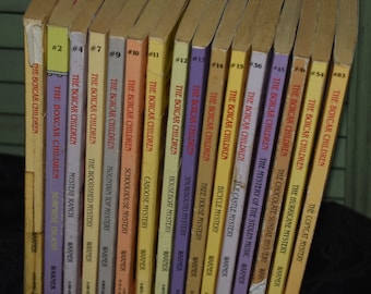 Puede incluir: Una colección de 15 libros de bolsillo con cubiertas amarillas, naranjas y moradas. Los libros se titulan "The Boxcar Children" y cada libro tiene un título de misterio diferente. Los libros están ordenados del #2 al #15.
