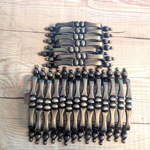 May include: A set of 18 antique brass cabinet knobs with a beaded design. The knobs are arranged in two rows, with the top row containing 9 knobs and the bottom row containing 9 knobs.