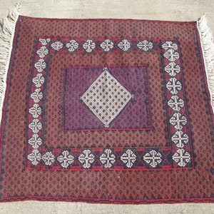 May include: A traditional rug with a burgundy, black, and white geometric pattern. The rug has a fringe border and is made of wool.