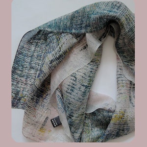 May include: A light blue and green silk scarf with a white and yellow abstract print. The scarf is folded and has a black tag with the text "Made in China" on it.