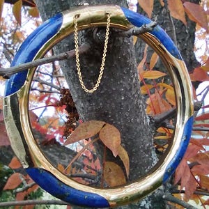 Puede incluir: Un brazalete de oro con un diseño de esmalte azul y dorado. El brazalete tiene una cadena.