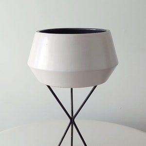 May include: White ceramic planter with a geometric shape, sitting on a black metal tripod stand.