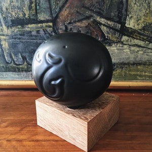 May include: A black ceramic sphere with a raised design on a wooden base. The sphere has a smooth, glossy finish.