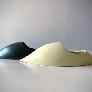 May include: Two ceramic planters shaped like a shoe. One planter is a dark green colour and the other is a light cream colour.