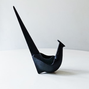 May include: A black ceramic bird sculpture with a long, thin neck and a curved body. The bird is perched on a white surface.