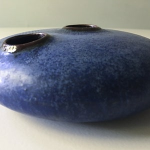 May include: A blue ceramic vase with two openings. The vase has a speckled glaze and a rounded shape.