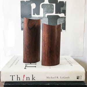 Może przedstawiać: Dwa zakrzywione, cylindryczne drewniane przedmioty w głębokim brązowym kolorze. Leżą na książce zatytułowanej "Think!" autorstwa Michaela R. LeGault. Tło przedstawia czarno-biały abstrakcyjny nadruk.