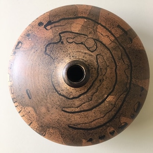 May include: A brown ceramic vase with black abstract designs. The vase has a round body and a small opening at the top.