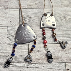 May include: Two silver metal shoe heel taps with beads hanging from them. The top heel tap says "Leo Tone Master" and the bottom heel tap says "Grif 210 Hell Tone Tap Trade Mark".