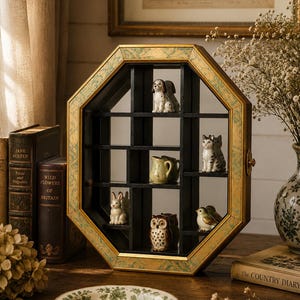 May include: An octagonal display shelf with a gold and green trim, holding miniature ceramic figurines. The shelf contains a dog, cat, rabbit, owl, and bird figurines, along with a small pitcher. Books and a decorative plate are in the foreground.