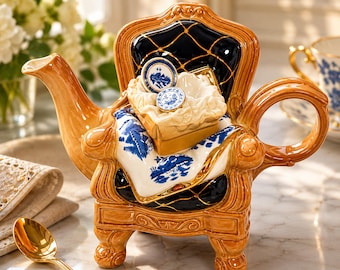 May include: A decorative teapot shaped like a chair, with a brown and black finish. The chair back is black with a diamond pattern. A white and blue patterned cloth is draped over the chair. Two small blue and white plates sit on top of a small box.