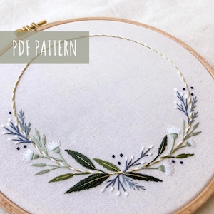 May include: A white embroidery hoop with a gold thread circle and a floral embroidery design in shades of green, blue, and white. The text "PDF PATTERN" is in the top left corner of the image.