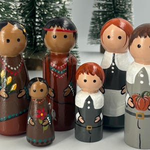 May include: Hand-painted wooden peg dolls depicting Native Americans and Pilgrims. The dolls feature detailed clothing and facial expressions, with vibrant colors and intricate designs. The set includes six figures, perfect for display or play.
