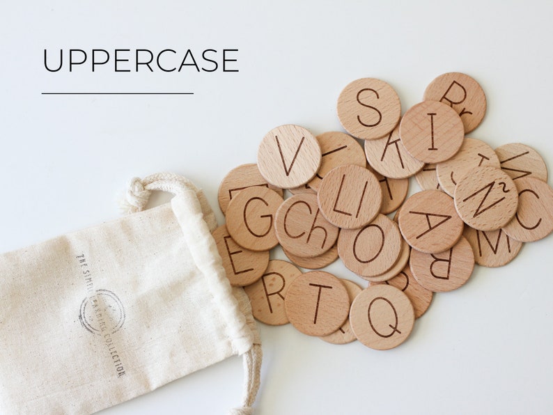 May include: A set of wooden alphabet letter tiles in a small white drawstring bag. The tiles are round and have the letters of the alphabet engraved on them. The letters are in uppercase. The bag has the text "The Simple  &  Natural Collection" printed on it.