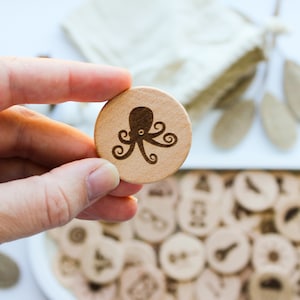 May include: A close-up of a wooden game piece with an octopus design. The piece is being held by a hand. The piece is part of a set of wooden game pieces.