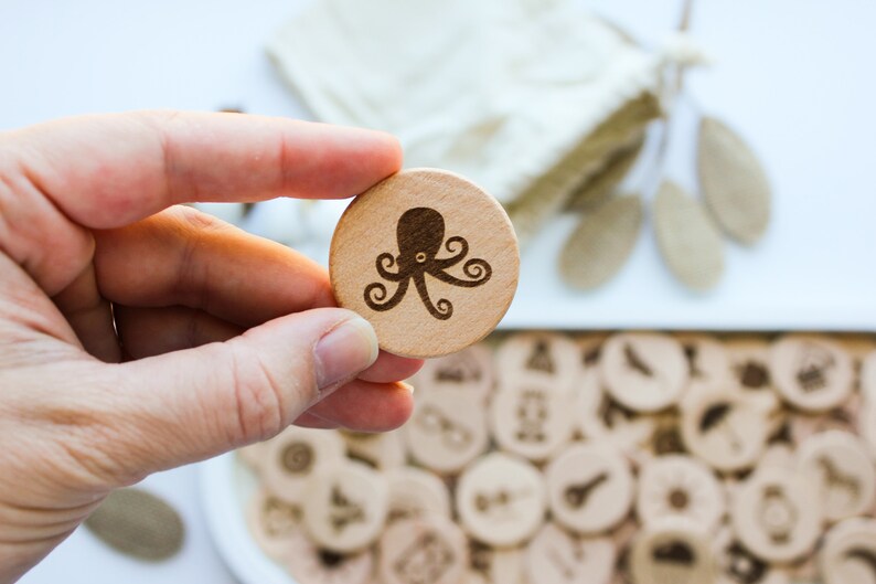 May include: A close-up of a wooden game piece with an octopus design. The piece is being held by a hand. The piece is part of a set of wooden game pieces.