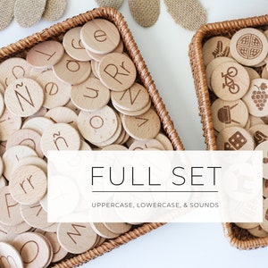 May include: Two wicker baskets filled with wooden alphabet and picture tiles. The baskets are on a white surface. The text "FULL SET UPPERCASE, LOWERCASE, & SOUNDS" is displayed on a white rectangle in front of the baskets.