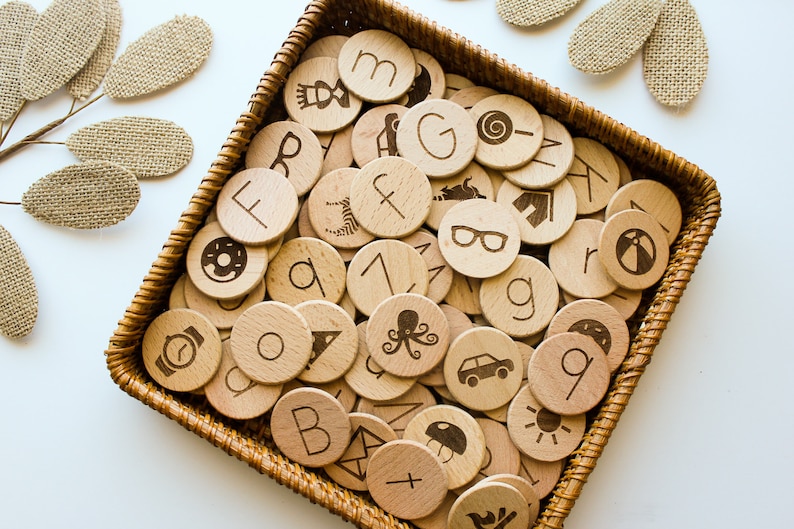 May include: A wicker basket filled with wooden circles, each with a different letter, number, or symbol engraved on it. The circles are arranged in a random pattern.