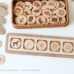May include: Wooden tray with five slots for letter tiles. The tray has the word "perro" spelled out with tiles. There are additional letter tiles and a basket of wooden tiles with various images on them.