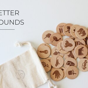May include: A set of wooden letter sound learning tokens in a white drawstring bag. The tokens feature various images, such as a bee, a car, a cow, a frog, a hand, a key, a tiger, and a bicycle. The bag has the text "The Simple Learning Collection" printed on it.