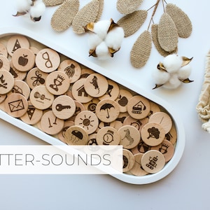 May include: Wooden tray filled with letter sound learning tokens. Each token features a different image, such as an apple, a key, and a sun. The tray is white and oval shaped. The text "LETTER-SOUNDS" is printed below the tray.