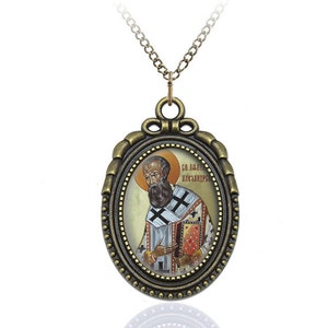 May include: A gold-toned oval pendant necklace with a religious icon of a man in a bishop's robe. The icon is surrounded by a gold-toned frame with a beaded edge. The text "Св. Иоанн Кронштадтский" is visible on the icon.